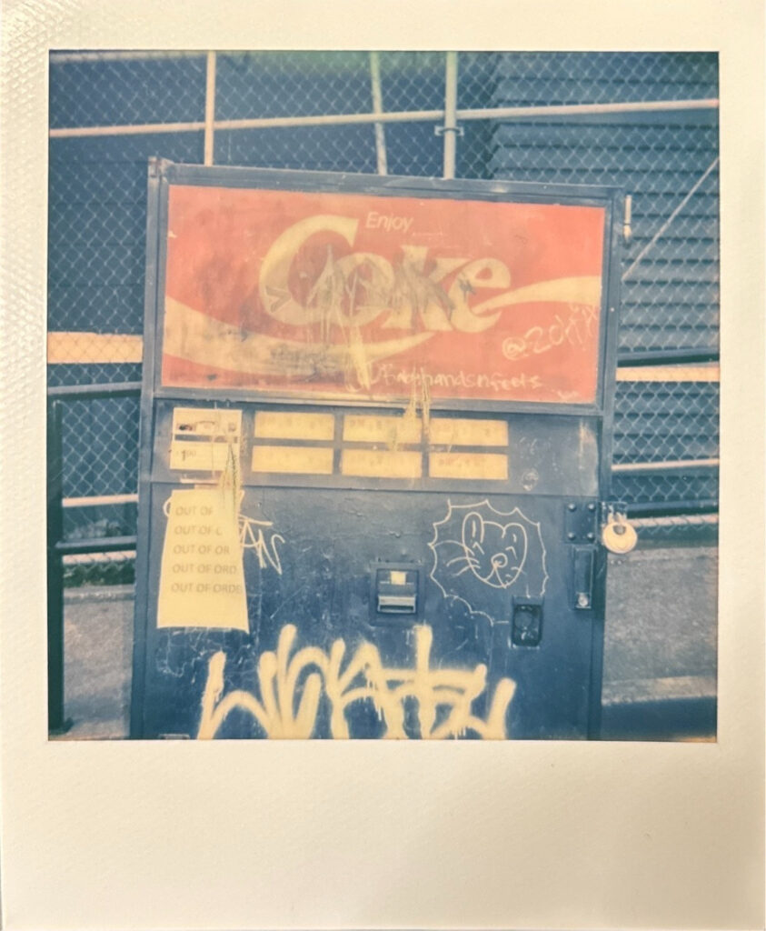 Polaroid of a graffitied Coke soda vending machine